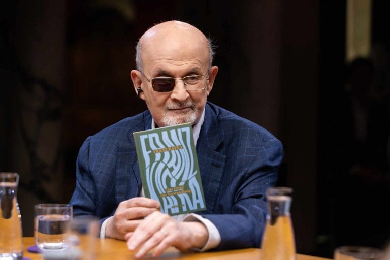 Sir Salman Rushdie sitzt unter der Lampe am Tisch des Literarischen Quartetts vom Mai 2024 und hält »Die Verwandlung« von Franz Kafka in der Hand (Foto: ZDF/Jens Gyarmati)